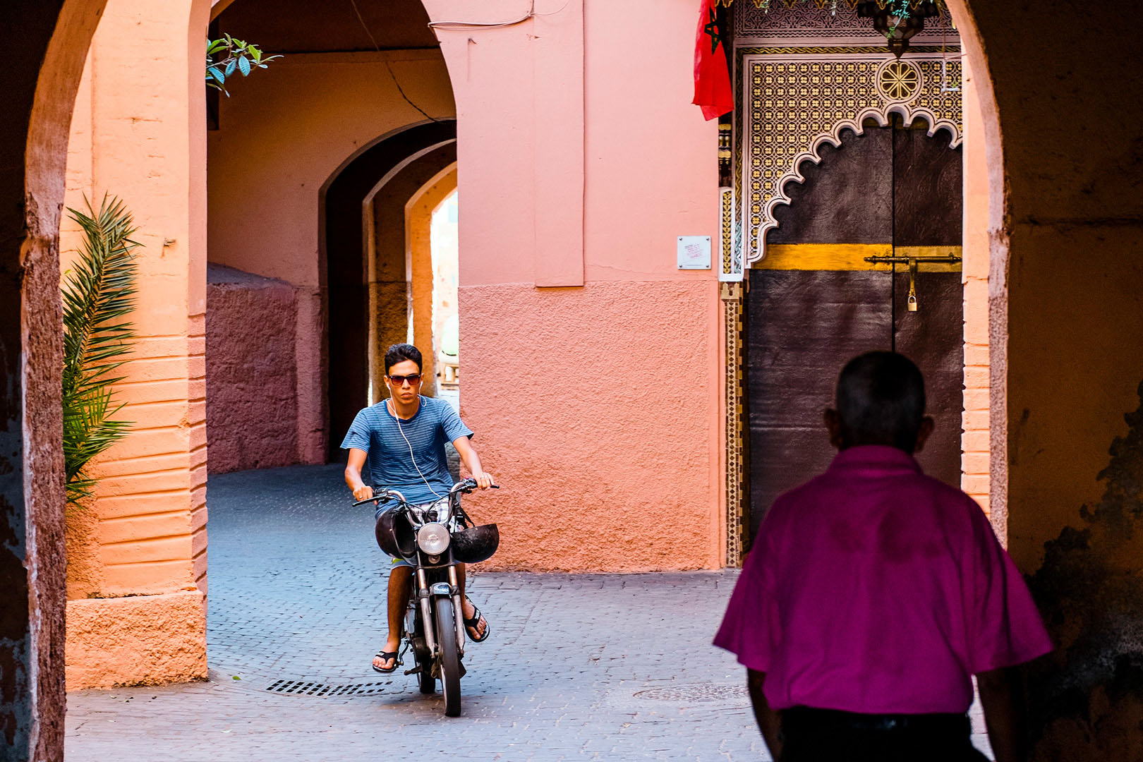 Man on scooter in colourful Marrakech sidestreet going under archway