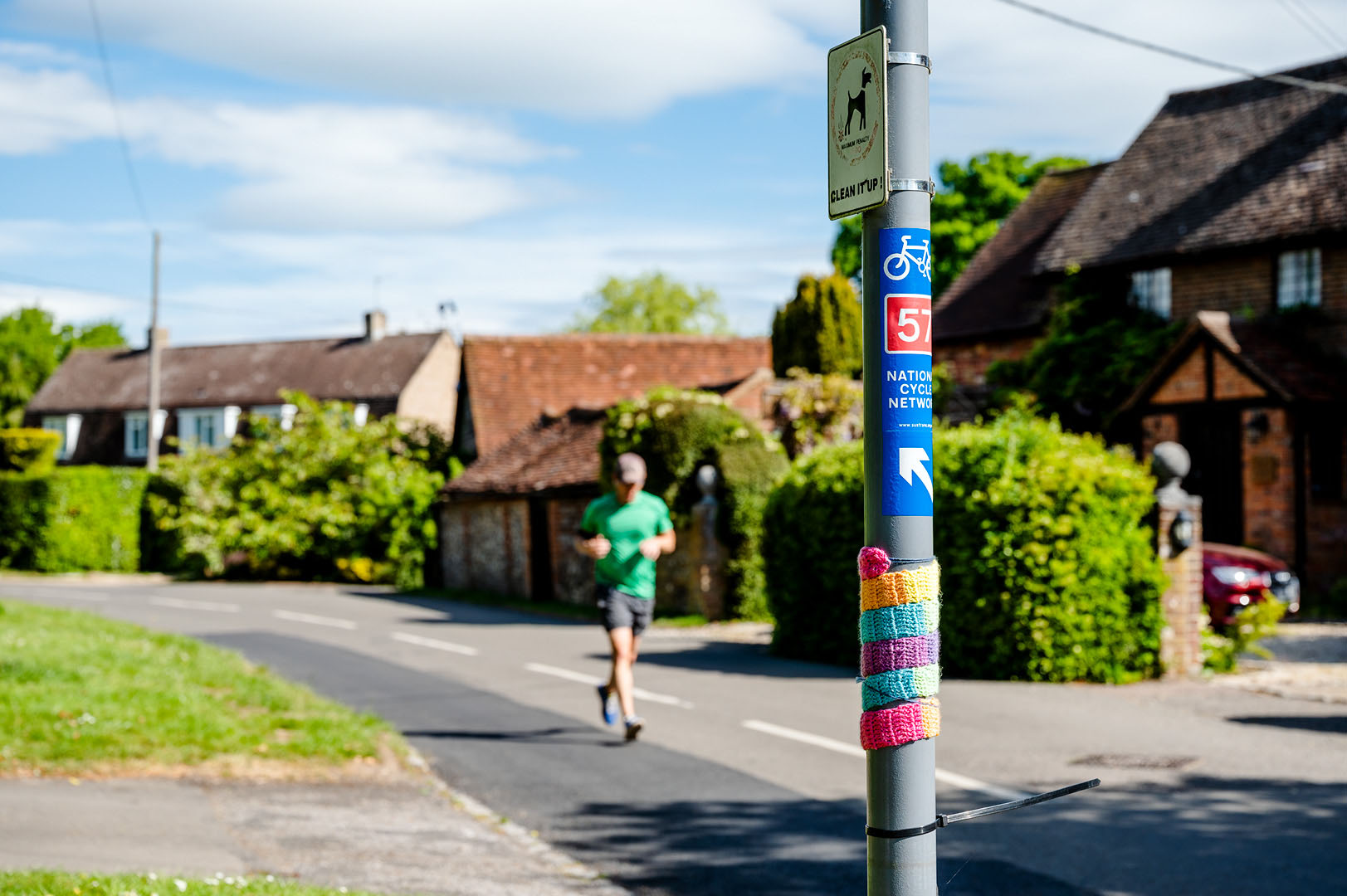 Solitary jogger on empty road passing rainbow adorned signpost during lockdown