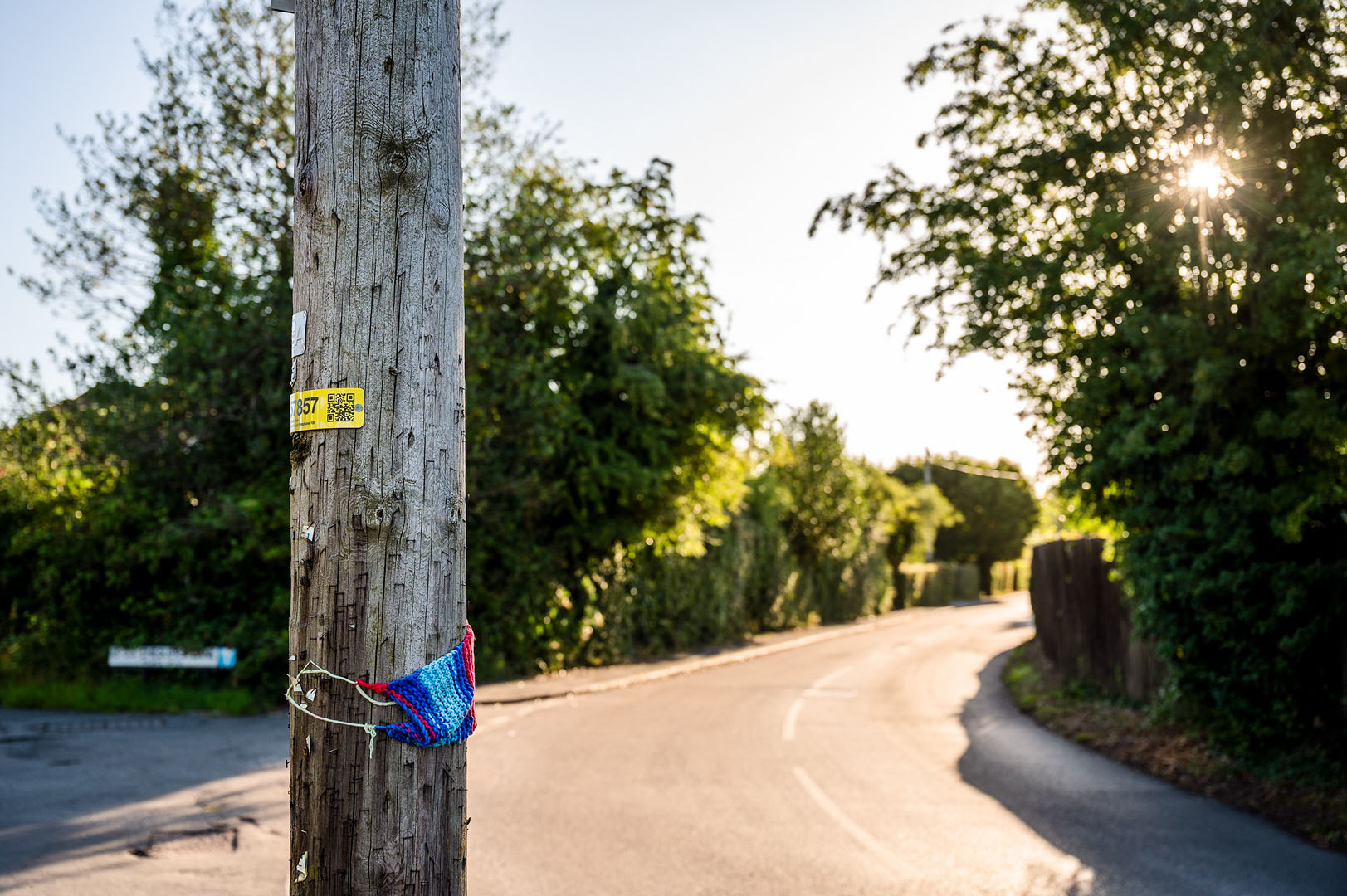 Knitted rainbow scarf attached to telegraph pole in deserted Rural road scene