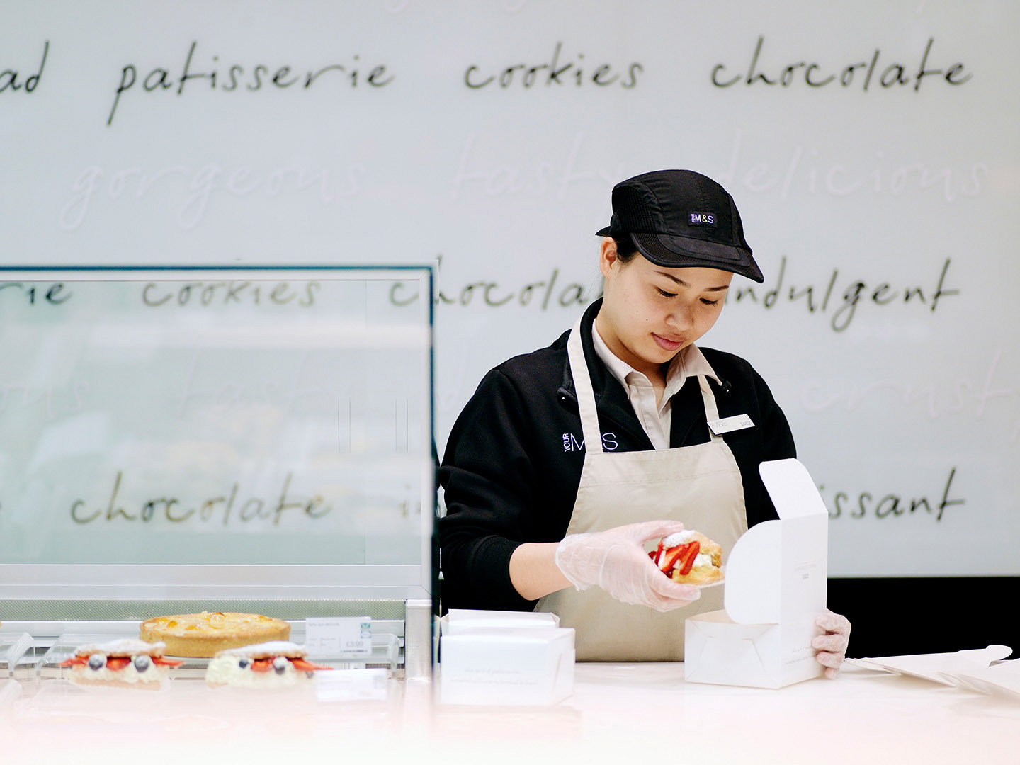 Woman putting patisserie in a box on shop counter