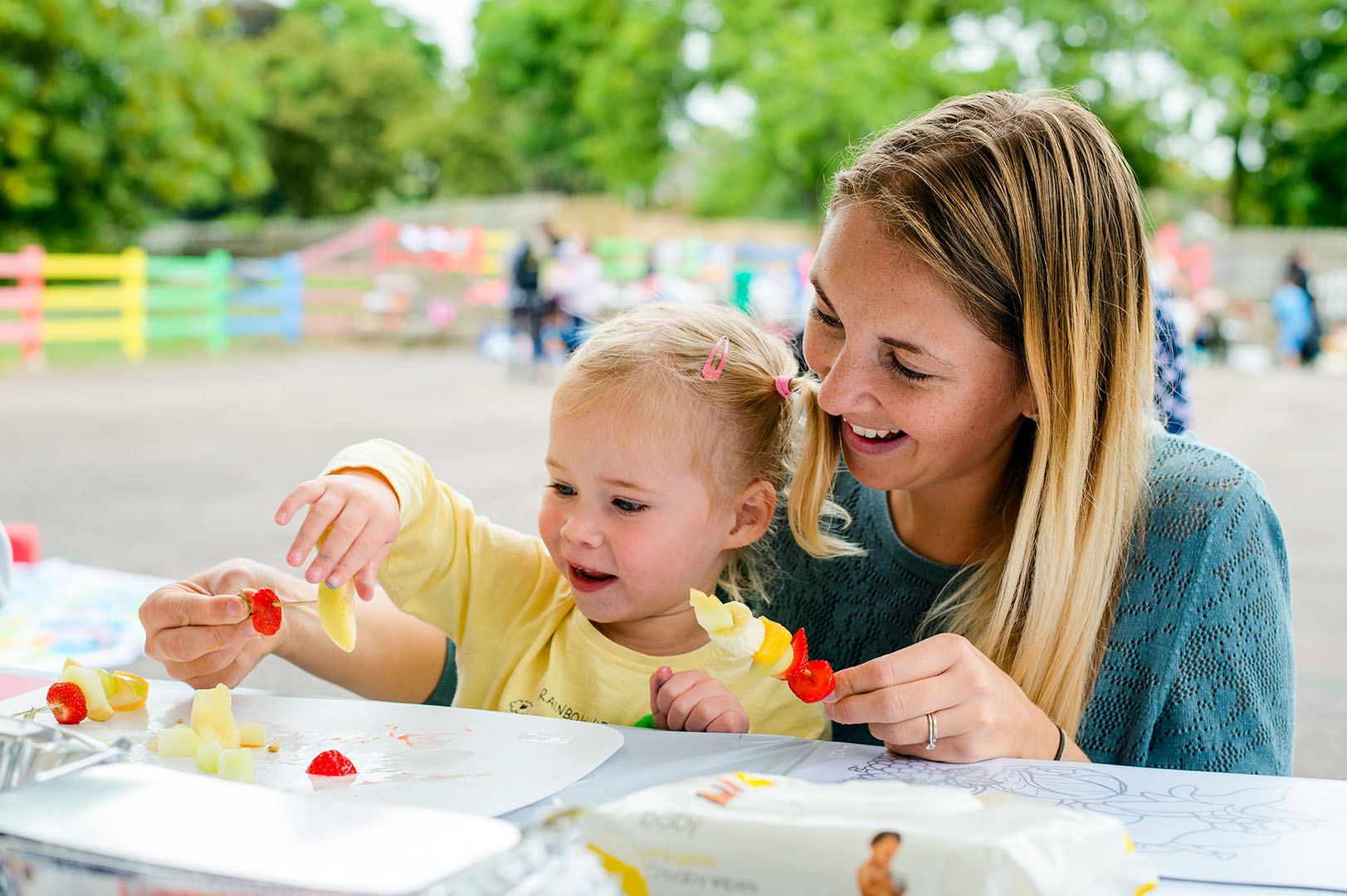 Mother & young child making fruit kebabs at community event