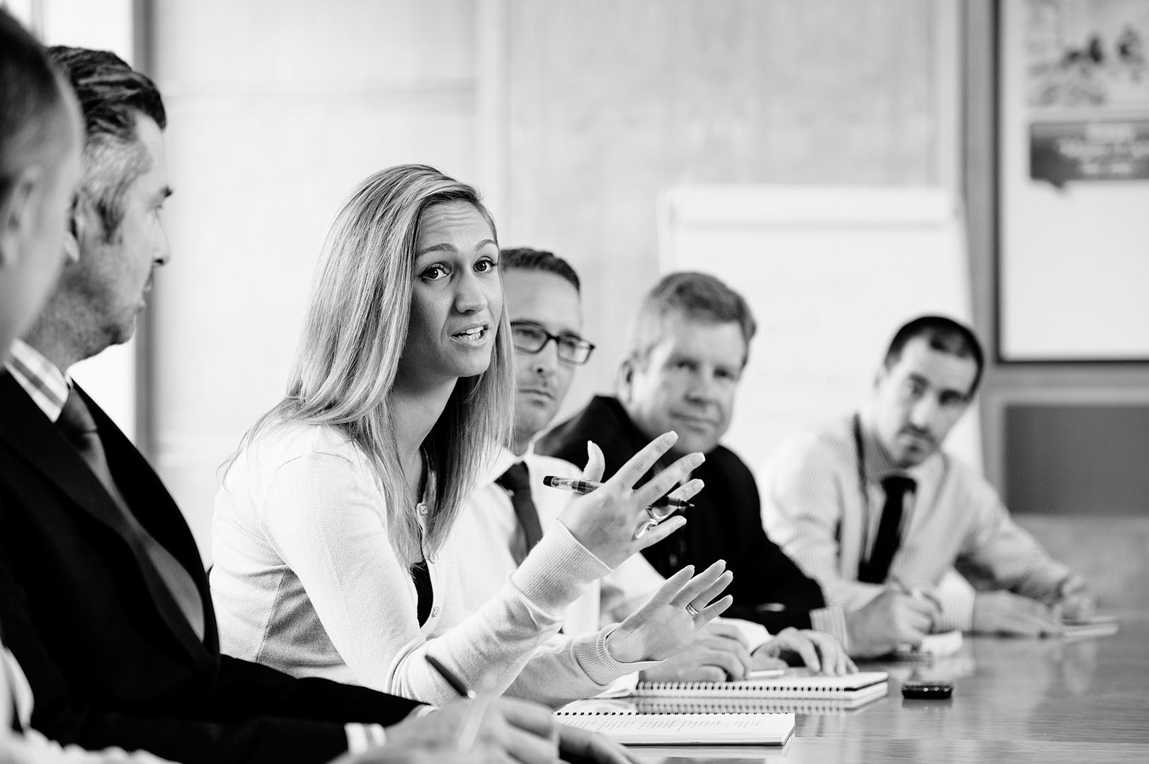 Woman leading the discussion surrounded by colleagues on long meeting room table