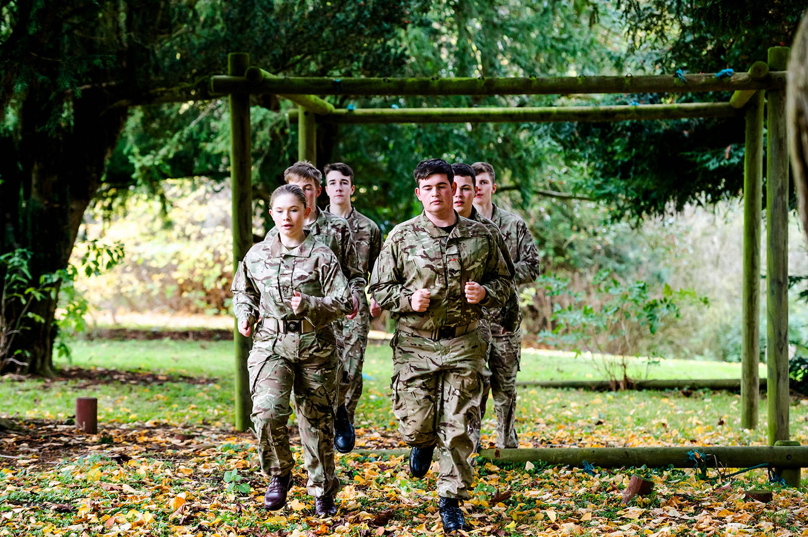 Group of army cadets jogging towards camera on woodland assault course