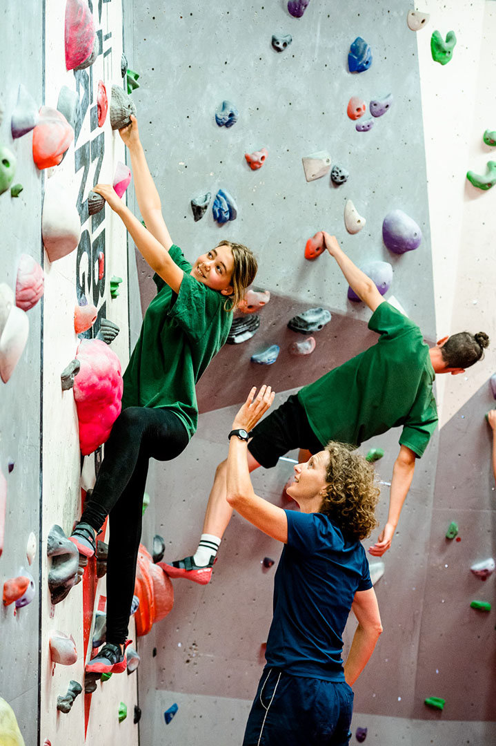 Female PE teacher in discussion with teenage female student on climbing wall