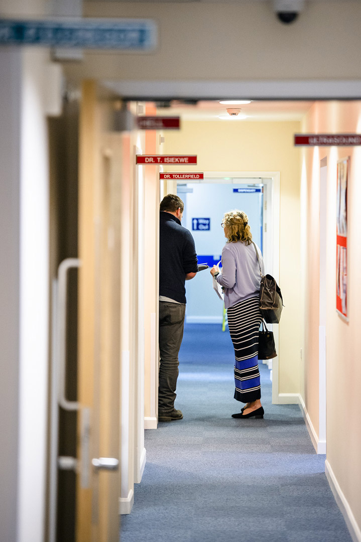 Two people full length in discussion from behind in Health Centre corridor