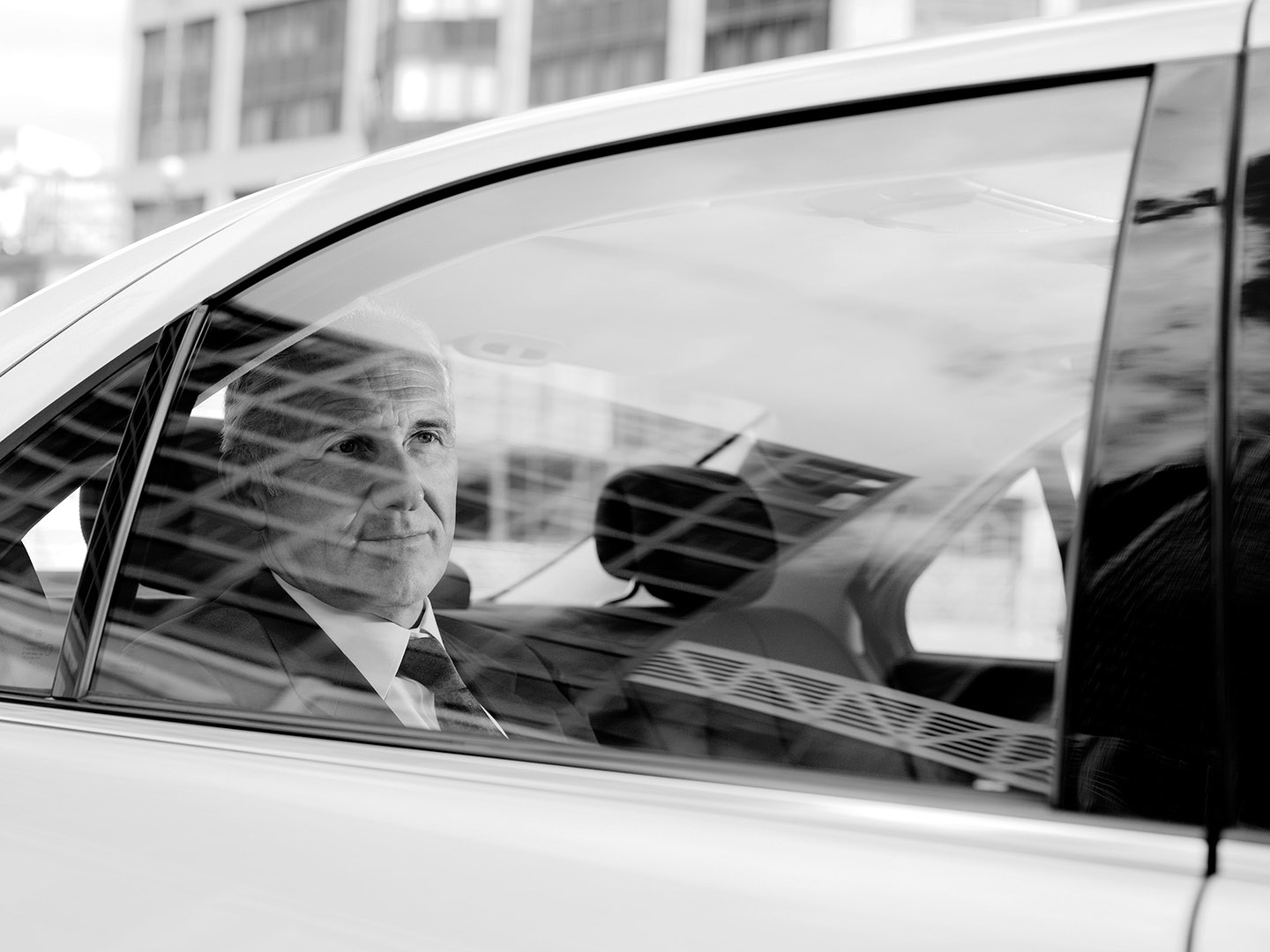 Businessman in back seat of Chauffer Driven car shot through the window with reflections