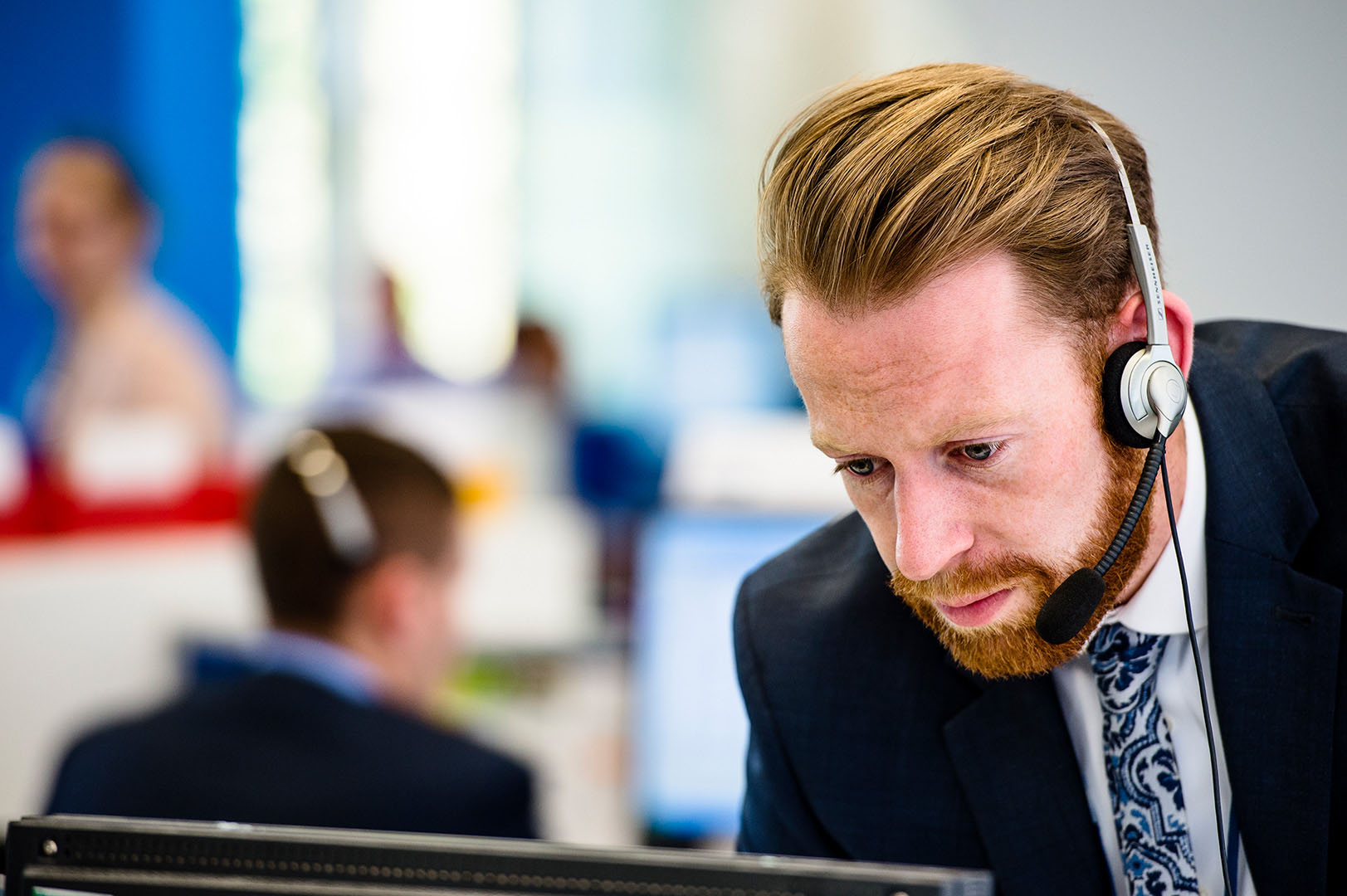 Man with headset leaning over looking at screen in customer support setting