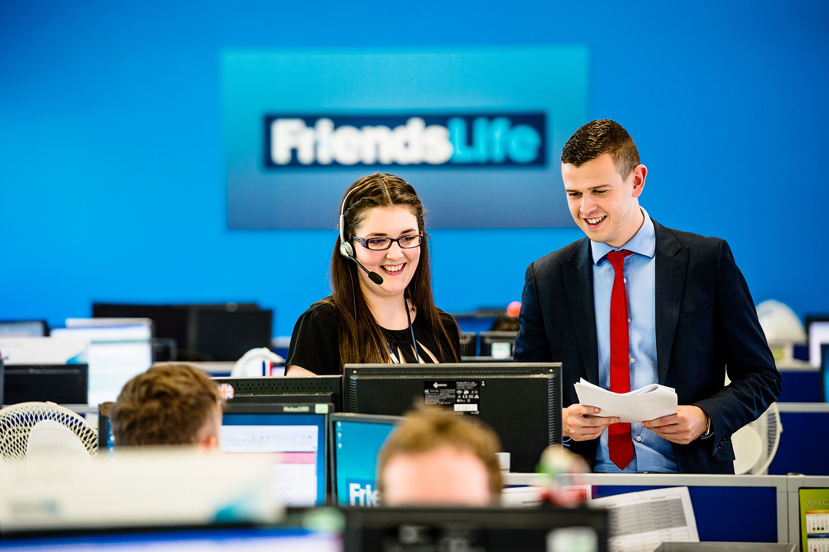 Two work colleagues, male and female, standing, in discussion looking at screen in corporate headquarters