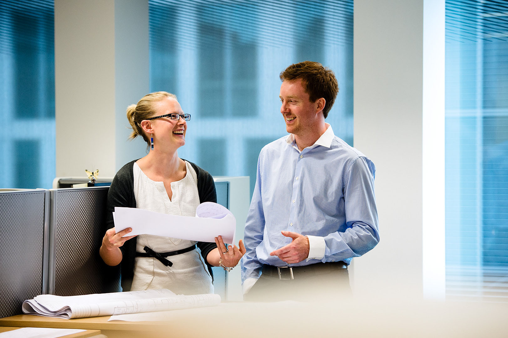 Two work colleagues, man and woman laughing and smiling in conversation in the office