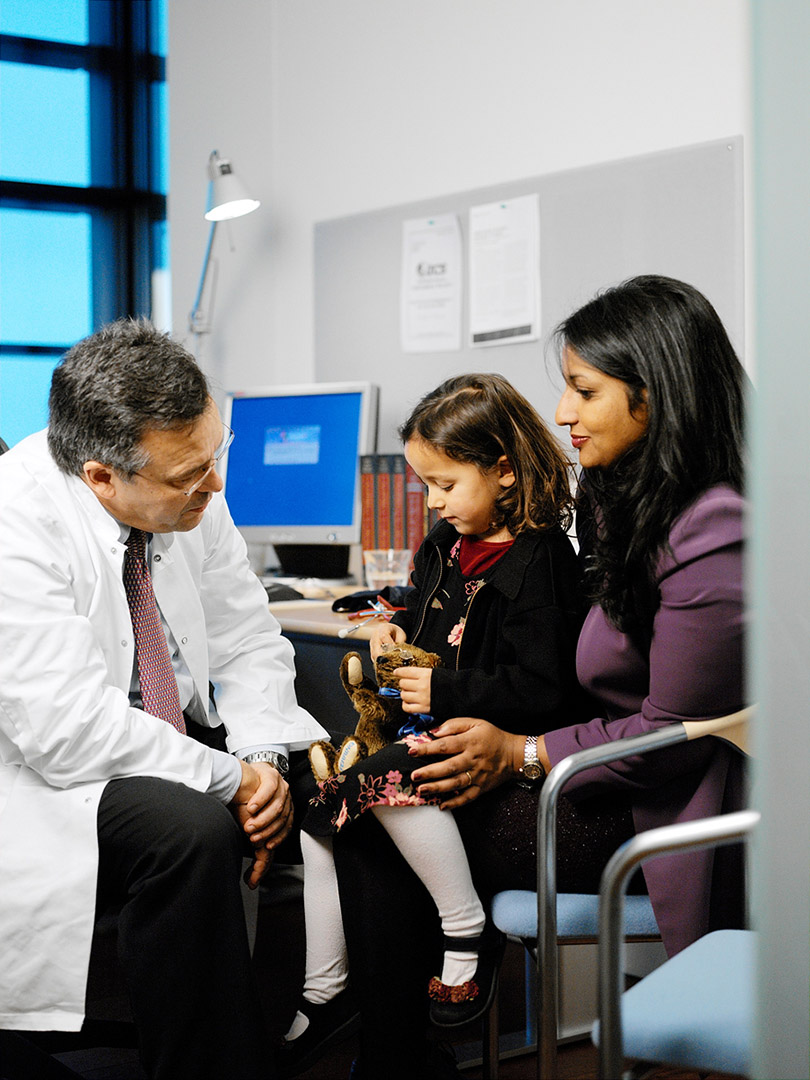 Asian mother & child in conversation with doctor in white coat in consulting room