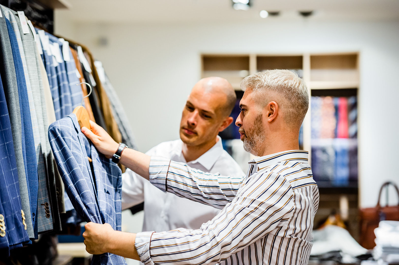Shop worker helping a customer choose a suit in fashion store