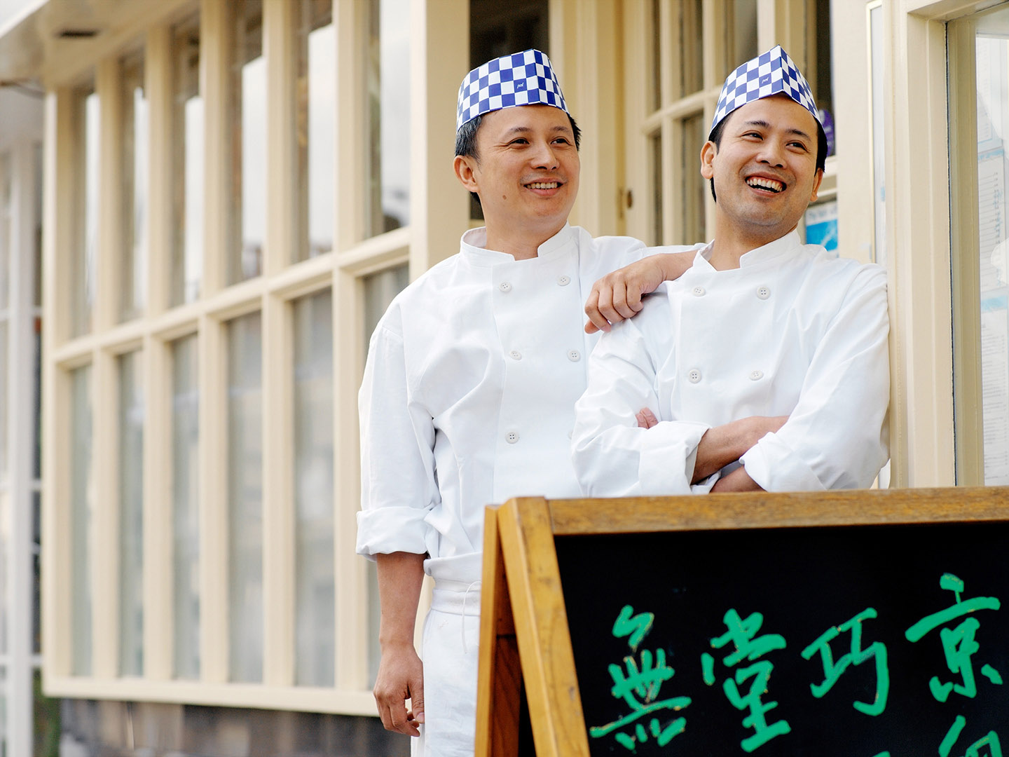 Two chefs smiling and laughing at the entrance to a Chinese restaurant