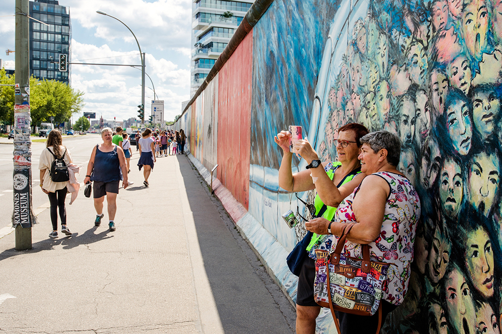 Two female tourists taking a selfie against a section of the Berlin Wall at Eastside Gallery