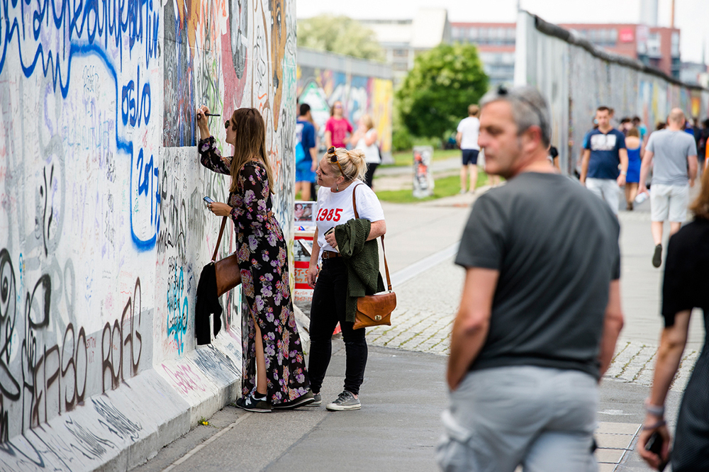 Girl in a long dress leaving her mark on the Berlin Wall at Eastside Gallery