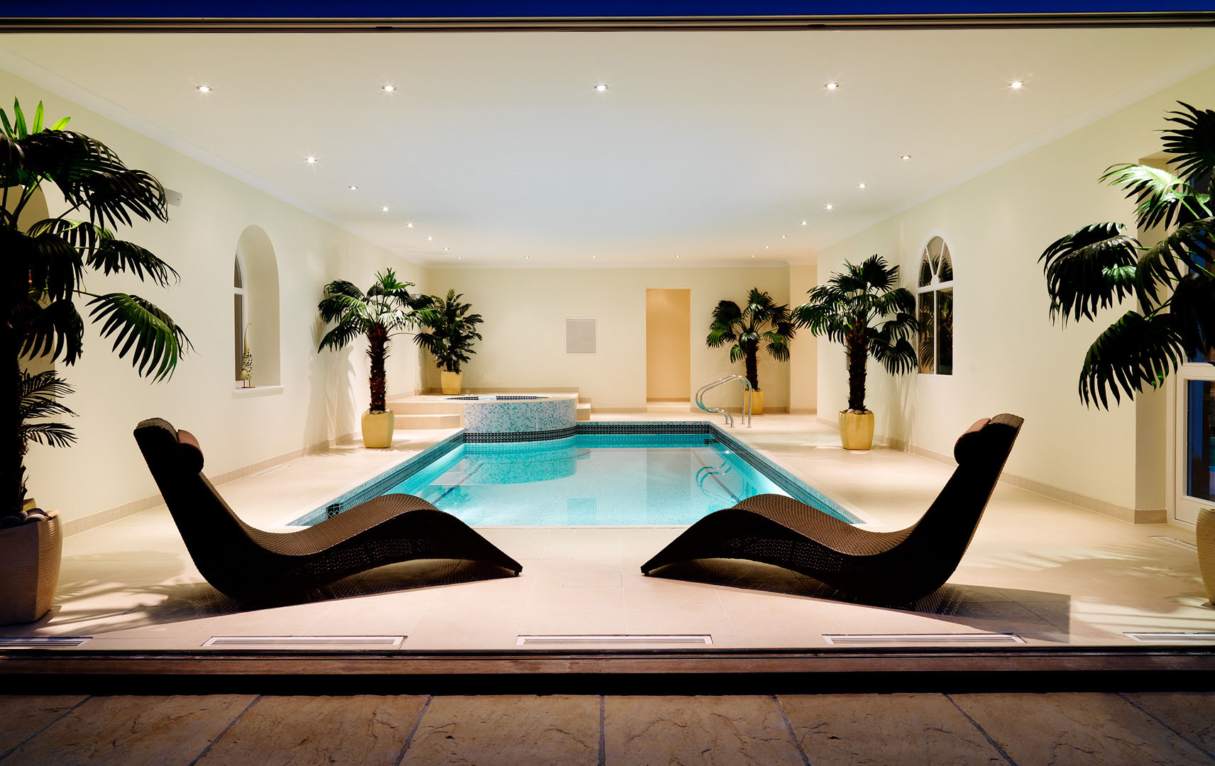 Interior with swimming pool in luxury property shot from opening doors to garden terrace