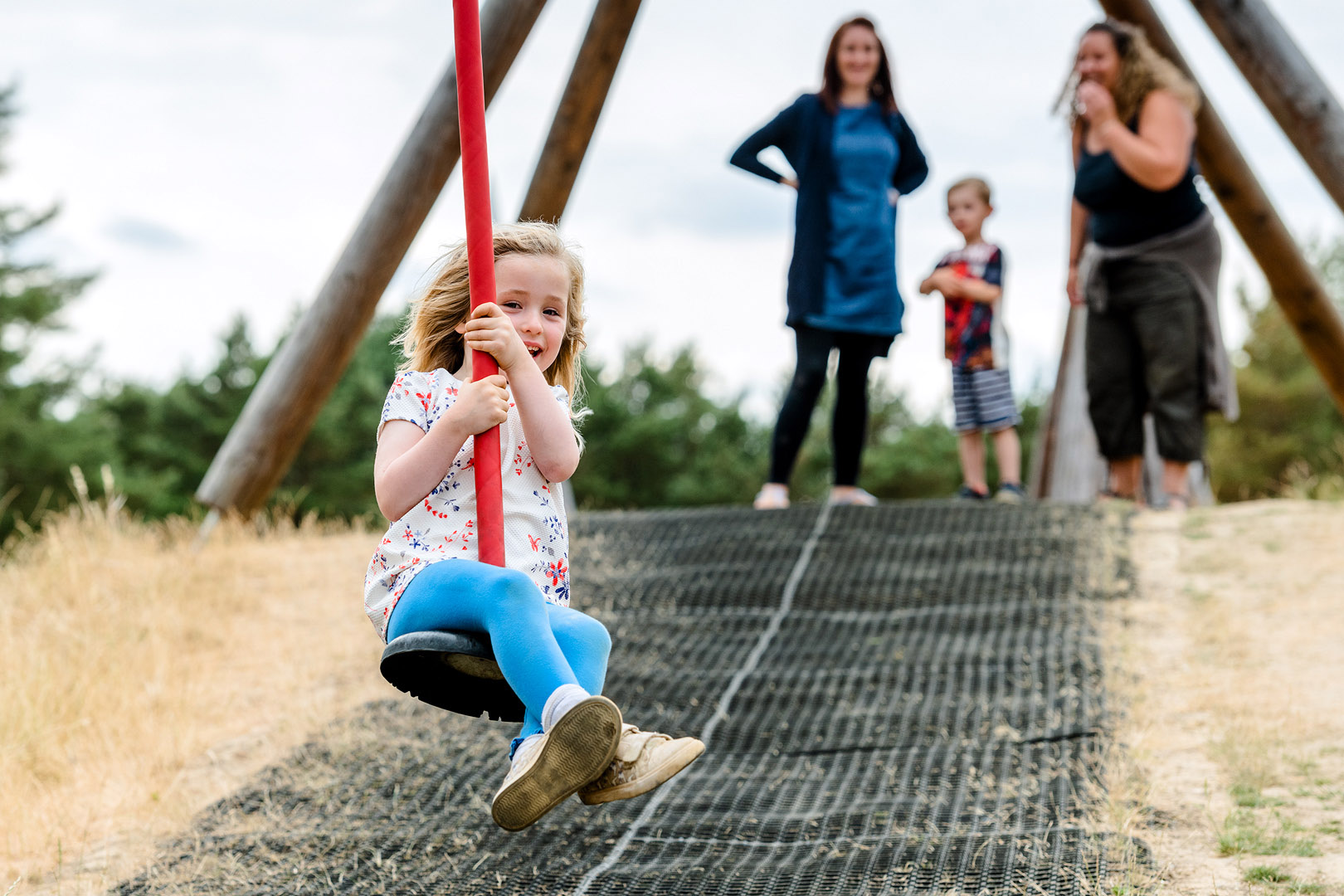 Young girl on zipwire coming towards camera with family watching in background