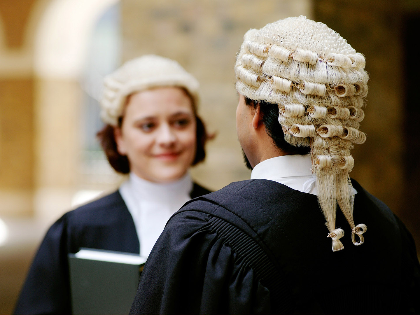Man in lawyers wig and gown shot from behind in conversation with female lawyer