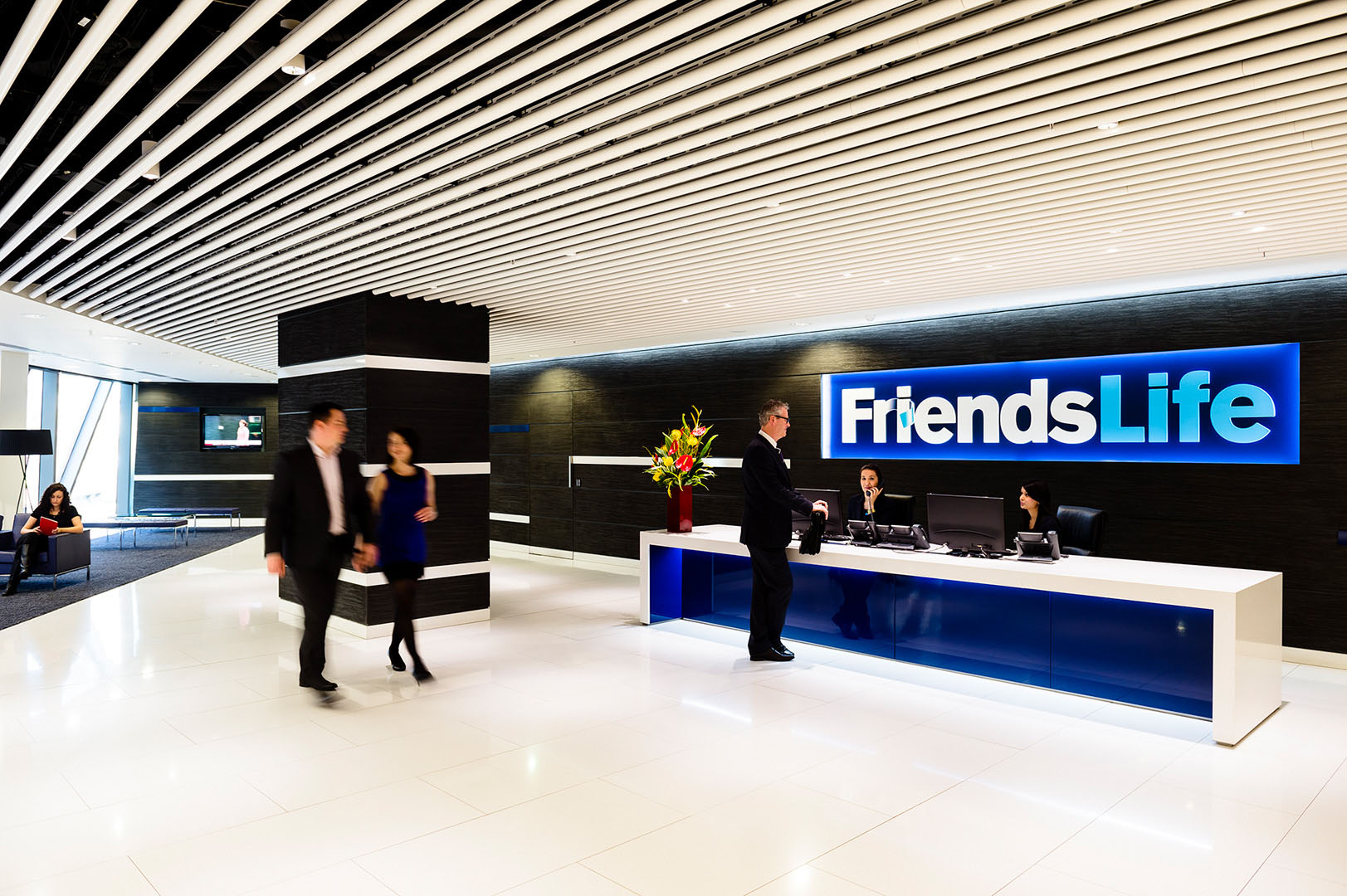 Man and woman in conversation as they walk through large reception of corporate office building