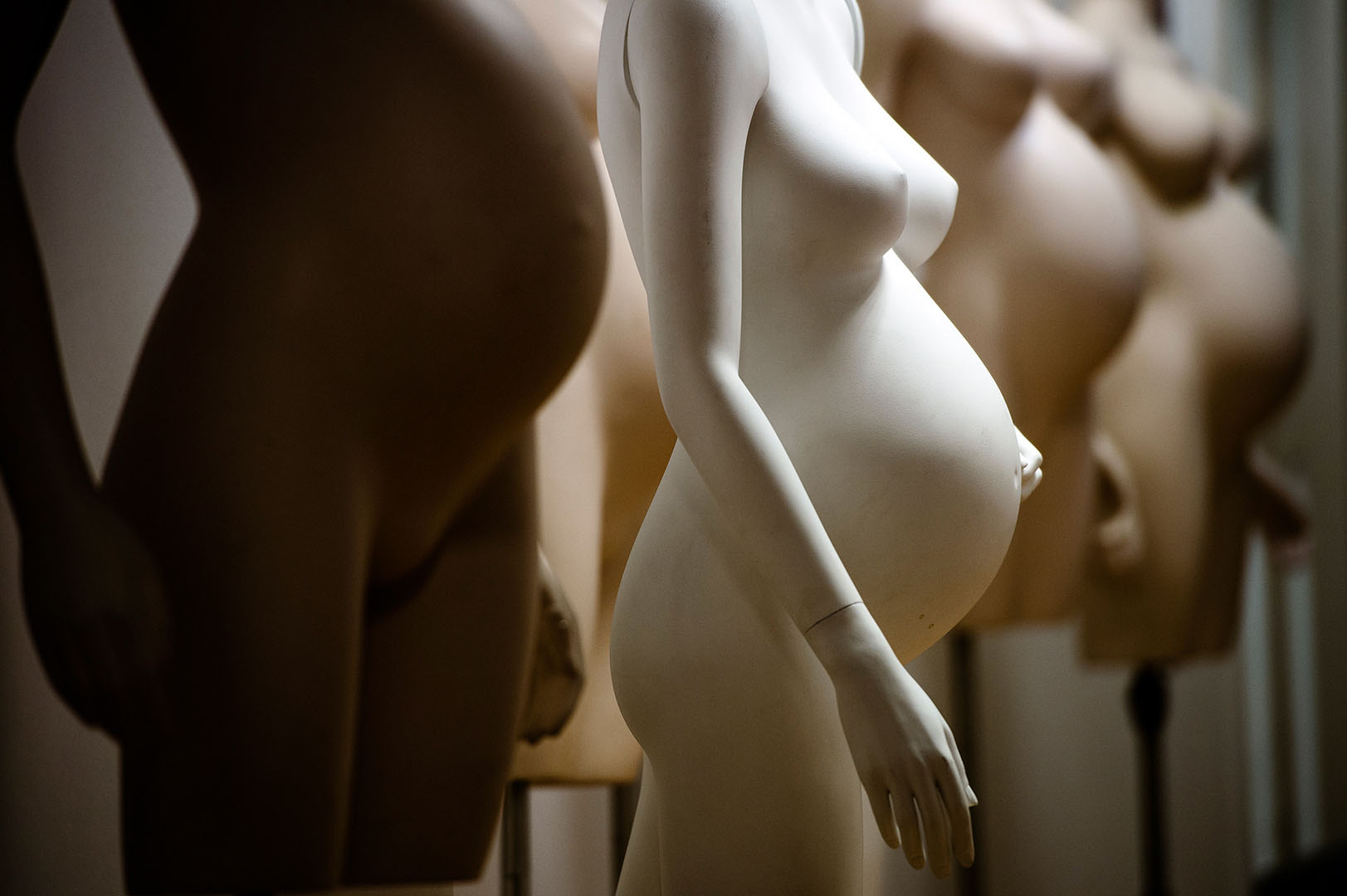 Undressed maternity mannequin amonsts others in store room