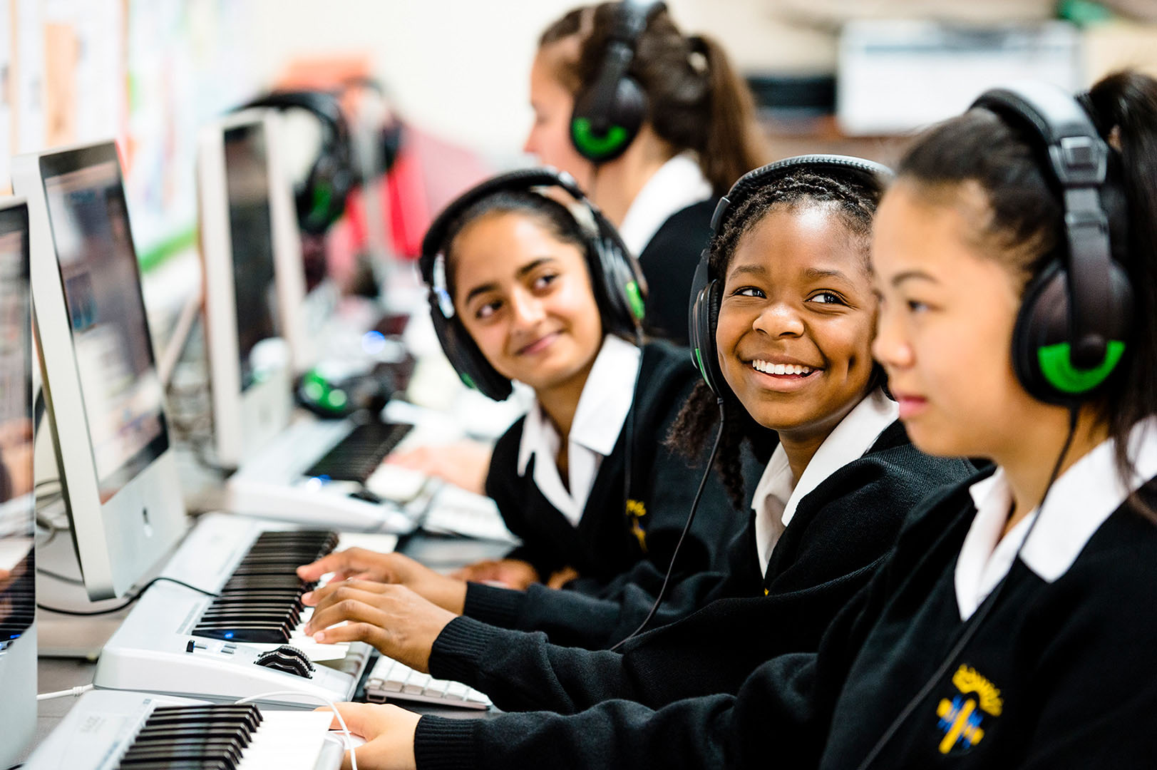 Mixed group of young female students having fun with keyboards & headphones in school music lesson