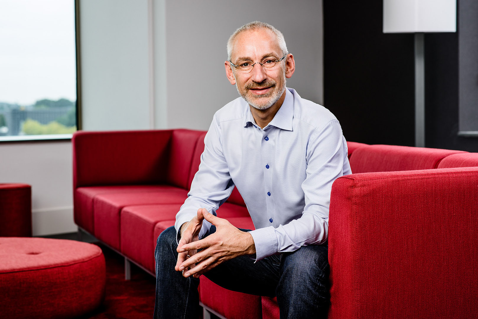 Male businessman sat on the edge of Sofa looking to camera