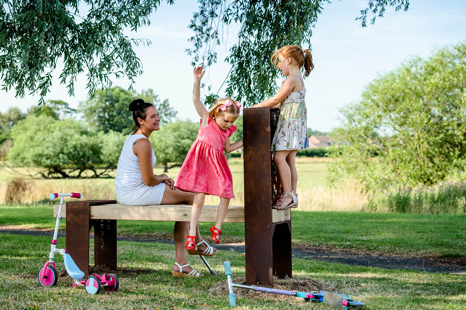 Two young girls with mother playing on park bench in rural setting