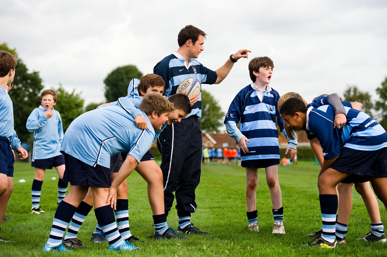Teenage schoolboys forming a scrum with coach in rugby training session