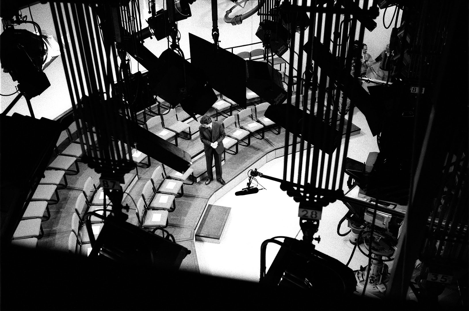Television panel discussion host checking audience details on chairs shot from above the lighting rig