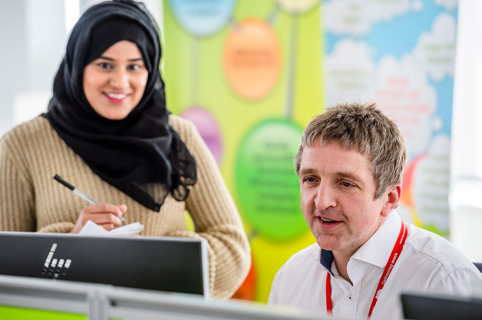 Woman in headscarf in conversation with male colleague looking at screen 