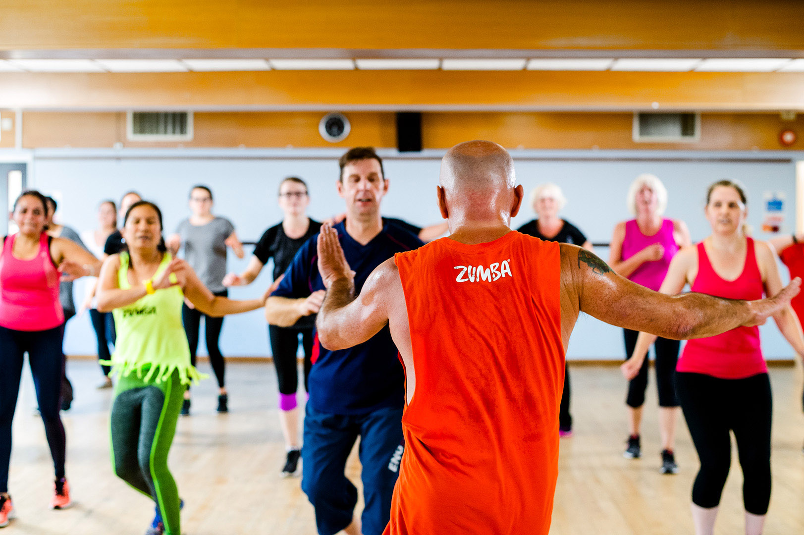 Zumba group session shot from behind bald headed perspiring tutor in motion