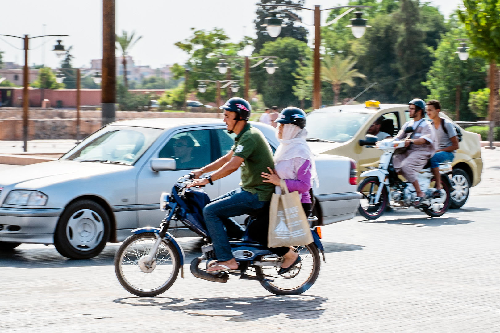 Two scooters with passengers in motion amongst traffic on Marrakech street