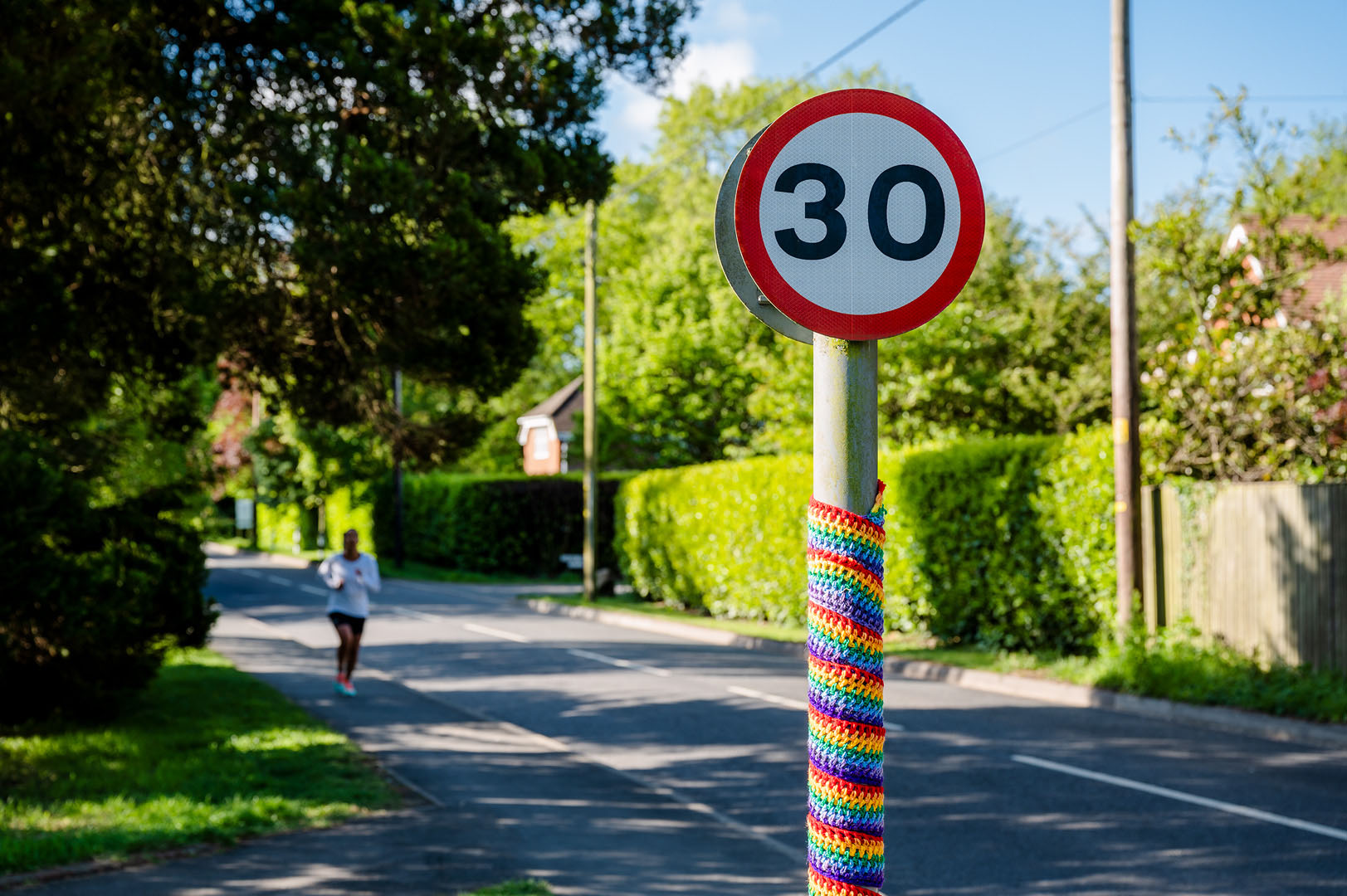 Rainbow adorned 30 mph sign on village road with jogger in the distance during Lockdown