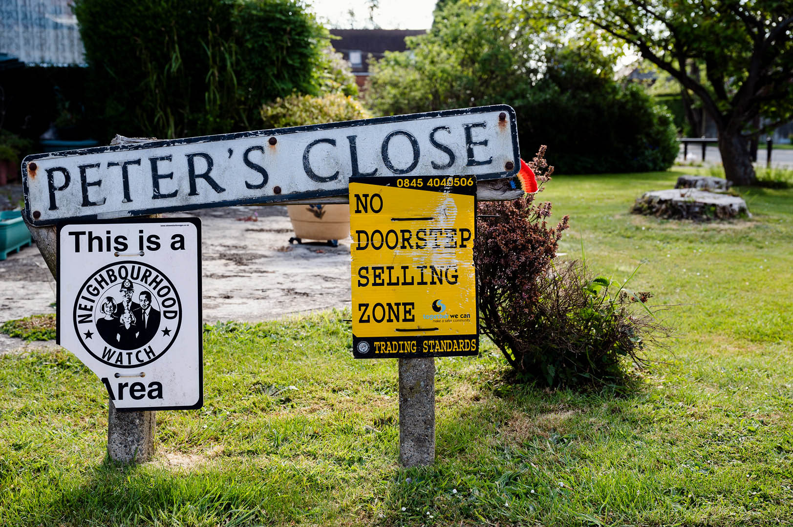 Knitted rainbow peeks from behind street sign with neighbourhood watch logo