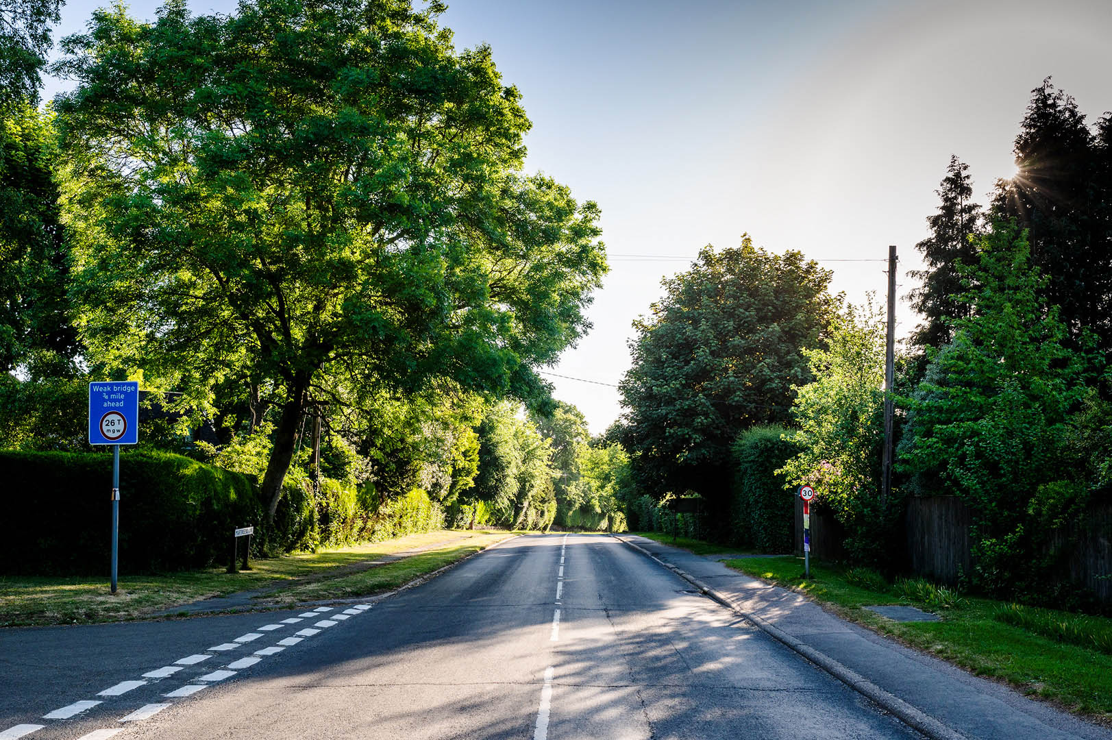 Deserted rural road scene with distant rainbow clad speed sign