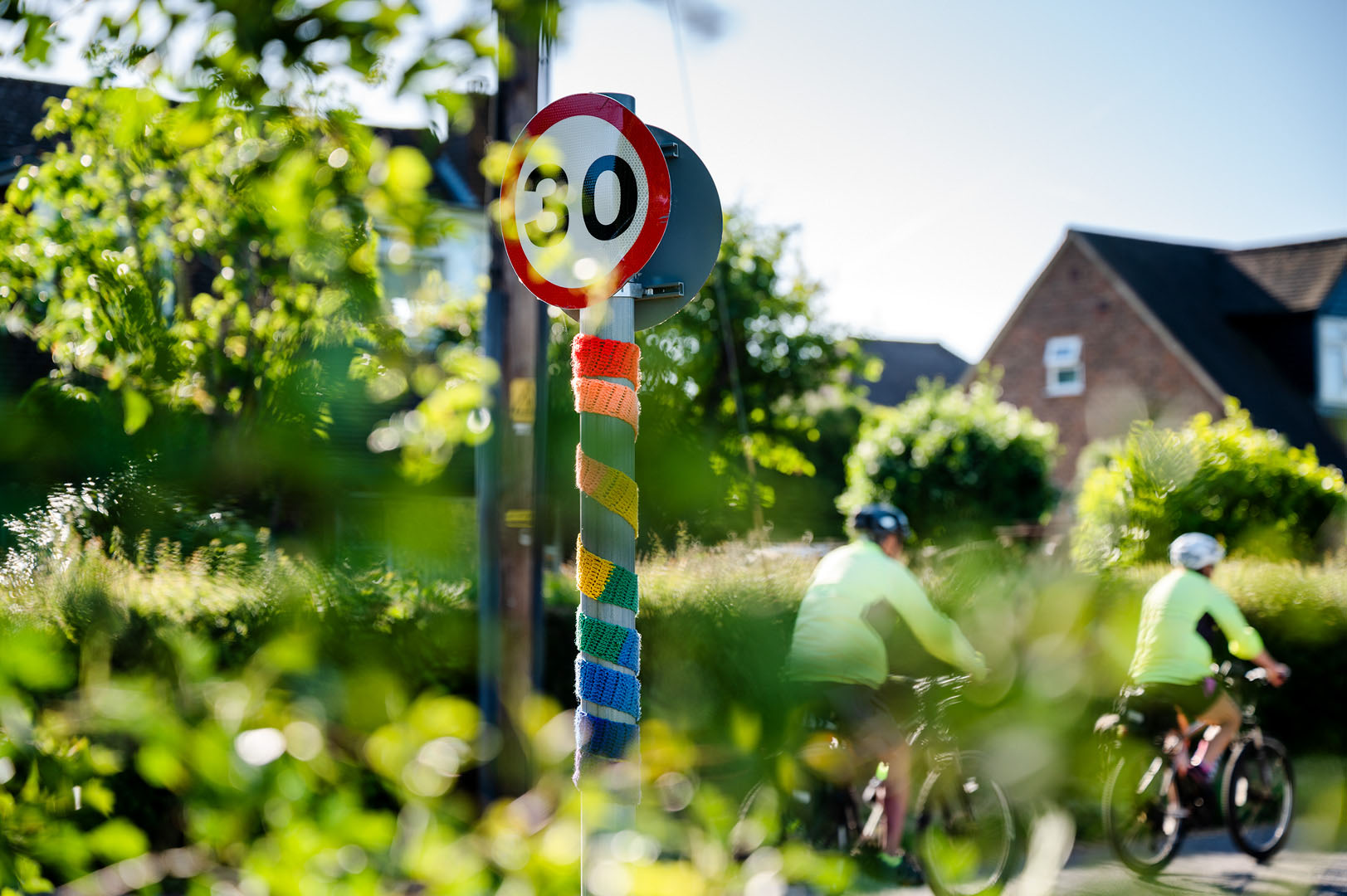 Rural speed sign wrapped in Rainbow scarf with cyclists passing during lockdown