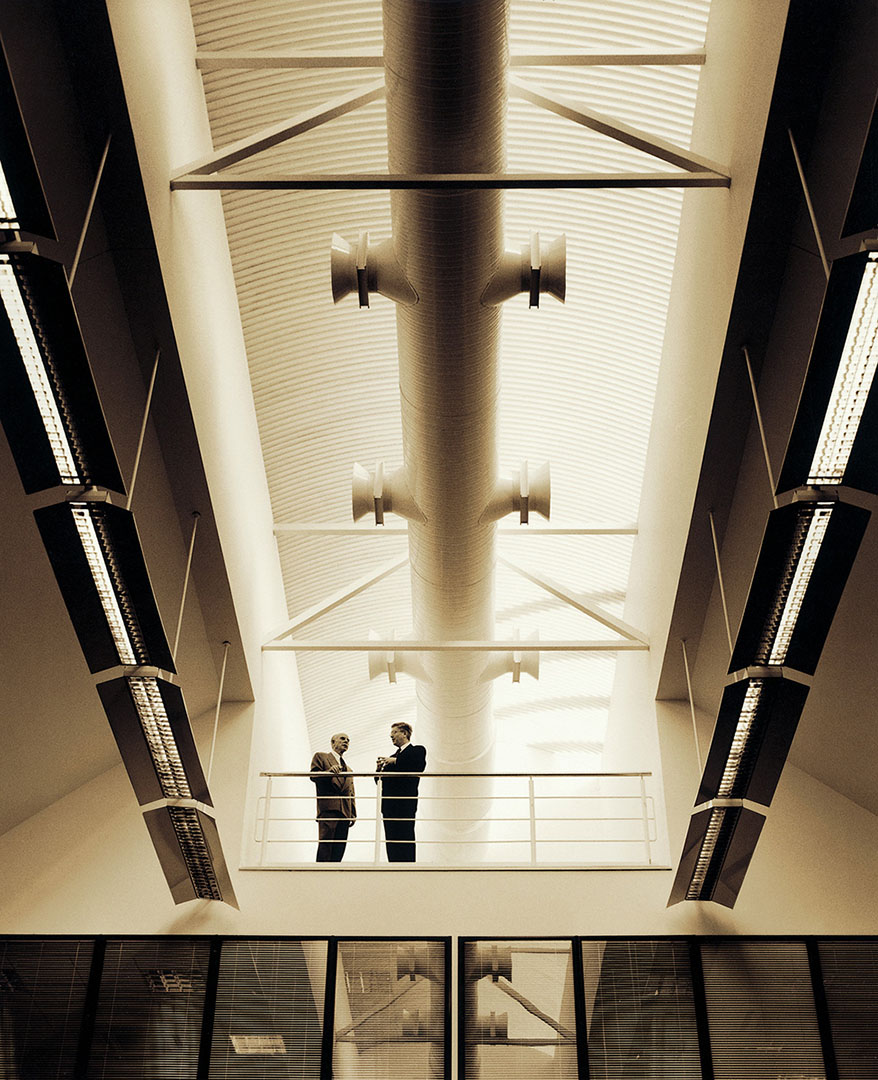 Two directors in discussion on balcony below large roof structure